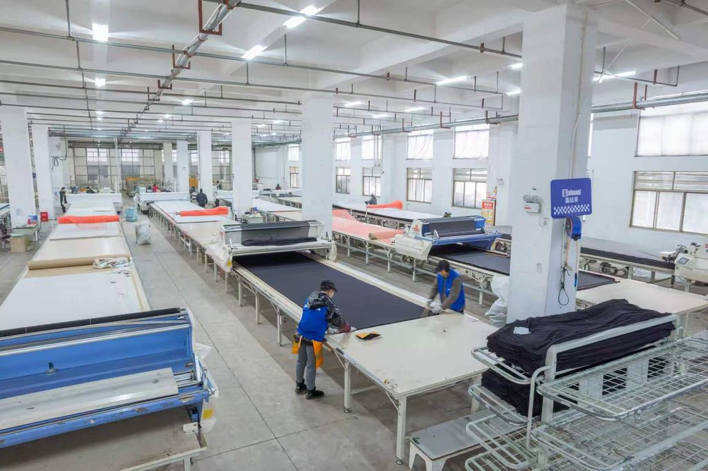 Workers handling dark fabric on long tables in the Gahumi workshop