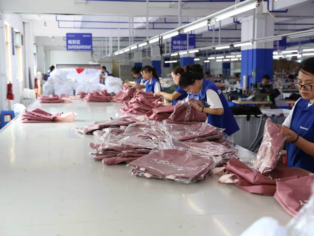 Workers packing pink printed tote bags at a long worktable